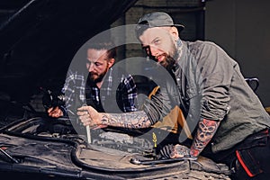 Two mechanics fixing car`s engine in a garage.