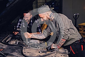 Two mechanics fixing car`s engine in a garage.