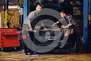 Two mechanics fixing car`s engine in a garage.