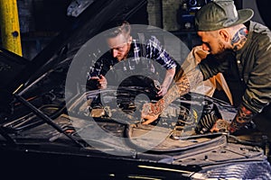 Two mechanics fixing car`s engine in a garage.