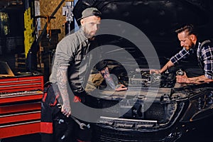 Two mechanics fixing car`s engine in a garage.