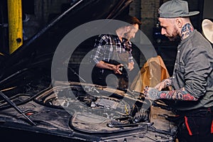 Two mechanics fixing car`s engine in a garage.