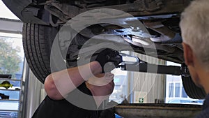 Two mechanics inspecting the bottom of the car with lamps on the service station