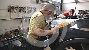 Two mechanics removing front bumper from car for repair in auto service. Professional repairmans dismantling automobile