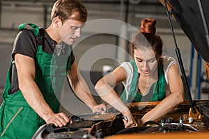 Two mechanics repair the engine of an orange car