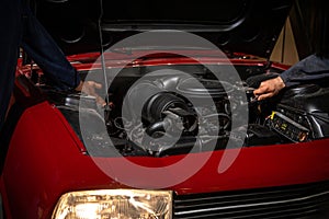 Two mechanics repair and maintain the engine of a red car