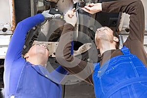 Two mechanics repairing a car in hydraulic lift