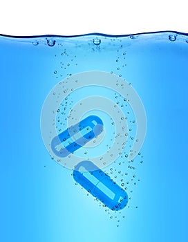 Two medical capsules dissolves in blue water photo