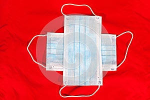 Two medical masks for one-use are on red background, laying in cross