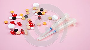 Two medical syringes and multi-colored pills lie on a pink background