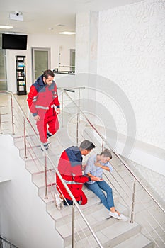 Two medical workers in red uniform coming to a woman on the stairs