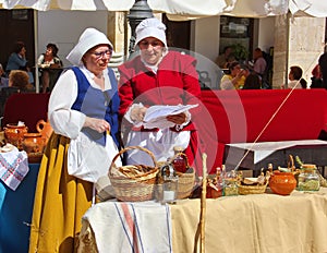 Two medieval peasant women in national Spanish costumes are trading in the market square