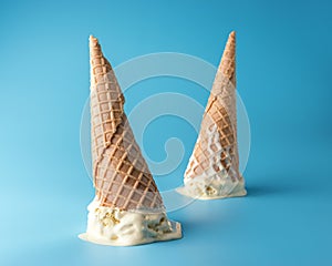 Two melted ice cream with ice cream cones on pastel blue background. Minimal summer food concept