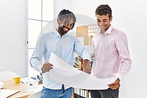 Two men architect workers smiling confident holding blueprint standing at architecture studio