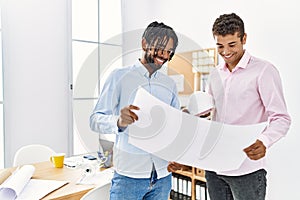 Two men architect workers smiling confident holding blueprint standing at architecture studio