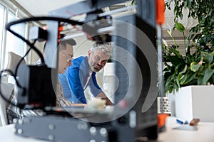 Two men architects using 3D printer in office and projecting house, drawing blueprints.