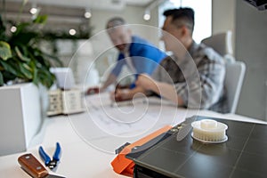 Two men architects using 3D printer in office and projecting house, drawing blueprints.