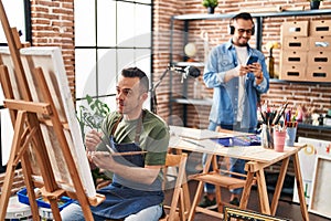 Two men artists smiling confident drawing and listening to music at art studio