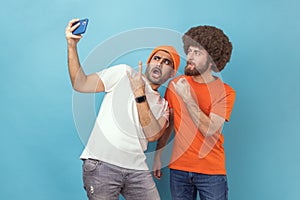 Two men blogger broadcasting livestream or taking selfie, showing rock and roll and shaka gestures.