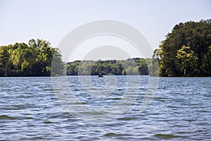 Two men on a boat fishing surrounded by the rippling blue water of Lake Lanier and lush green trees and plants