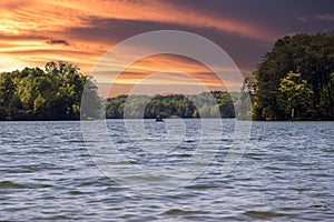 Two men on a boat fishing surrounded by the rippling blue water of Lake Lanier and lush green trees and plants