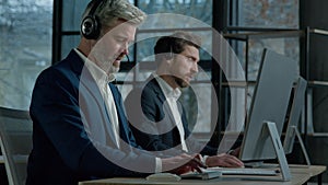 Two men call center service operators work in office talk to client using headset on computer concentrated sales agents
