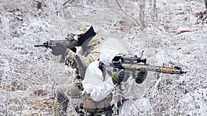 Two men in camouflage white, green uniform with machineguns back to back. Soldiers with muchinegun stood on knelt in the winter gr