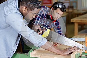 two men in carpentry workshop one using handsaw