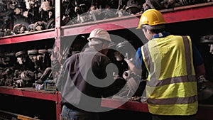 Two men checking engine parts in a warehouse. With both of them wearing helmets during working time, most of the products are mach