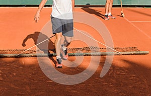 Two men clean tennis clay court