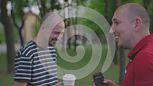 Two men communicate in a city park and drink coffee from disposable plastic glasses