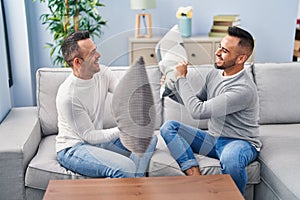 Two men couple fighting with cushion sitting on sofa at home