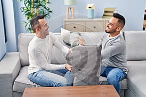 Two men couple fighting with cushion sitting on sofa at home