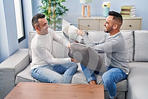 Two men couple fighting with cushion sitting on sofa at home