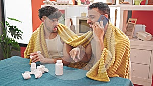 Two men couple having medical phone consultation at dinning room