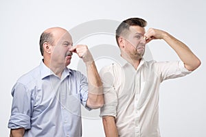 Two men cover their noses due to a bad smell