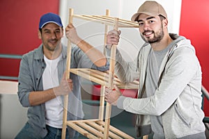 two men coworkers carry wood shelf