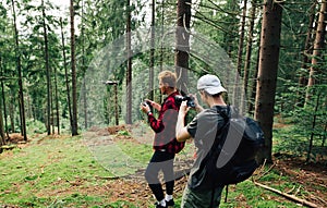 Two men create a video concentrate on a hike  a man shoots on camera as a friend flies a drone in a beautiful mountain forest.