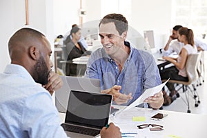 Two men discussing business documents in a busy office