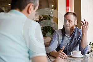 Two men discussing difficult issues with emotions during coffee break in cafe talking about problems of business negotiation