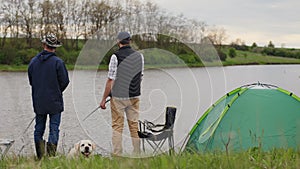 Two men with a dog are fishing on the lake