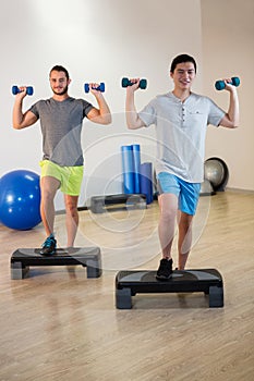 Two men doing step aerobic exercise with dumbbell on stepper