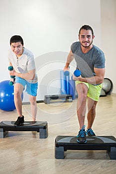 Two men doing step aerobic exercise with dumbbell on stepper