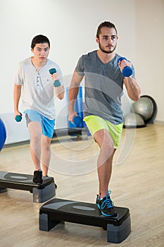 Two men doing step aerobic exercise with dumbbell on stepper