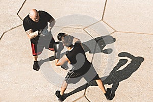 Two men exercising and fighting in outside. Boxer in gloves is training with a coach