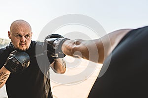 Two men exercising and fighting in outside. Boxer in gloves is training with a coach