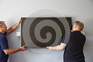 Two Men Fitting Flat Screen Television To Wall