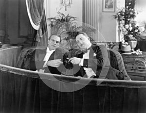 Two men in formal attire sitting together in a theater box