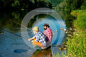 Two men friends anglers fishing. Flyfishing angler makes cast, standing in river water. Old and young fisherman.