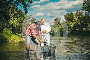 Two men friends fisherman fishing on river. Old father and son anglers with rod fishing at riverside. Recreational